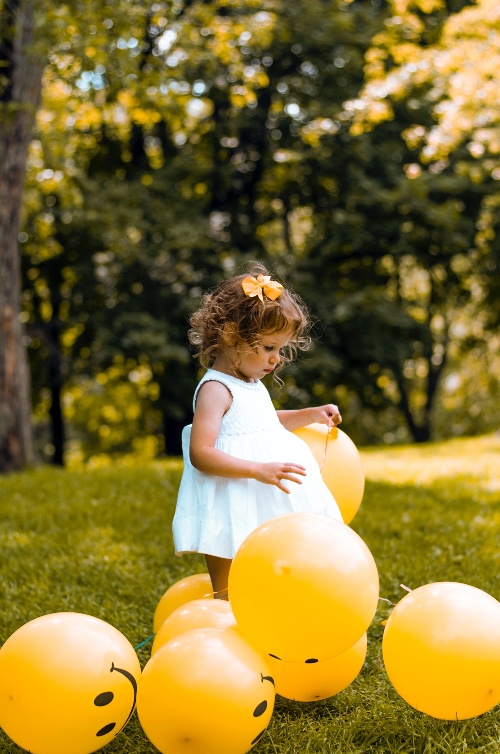 Klein meisje omringd door smileyballonnen in de natuur